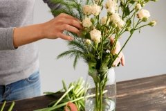 Girl make bouquet over gray background, putting flowers in vase.